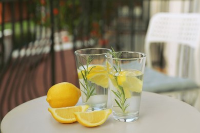 Glasses with refreshing lemon water and citrus fruits on light table outdoors