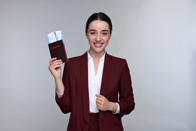 Smiling businesswoman with passport and tickets on grey background