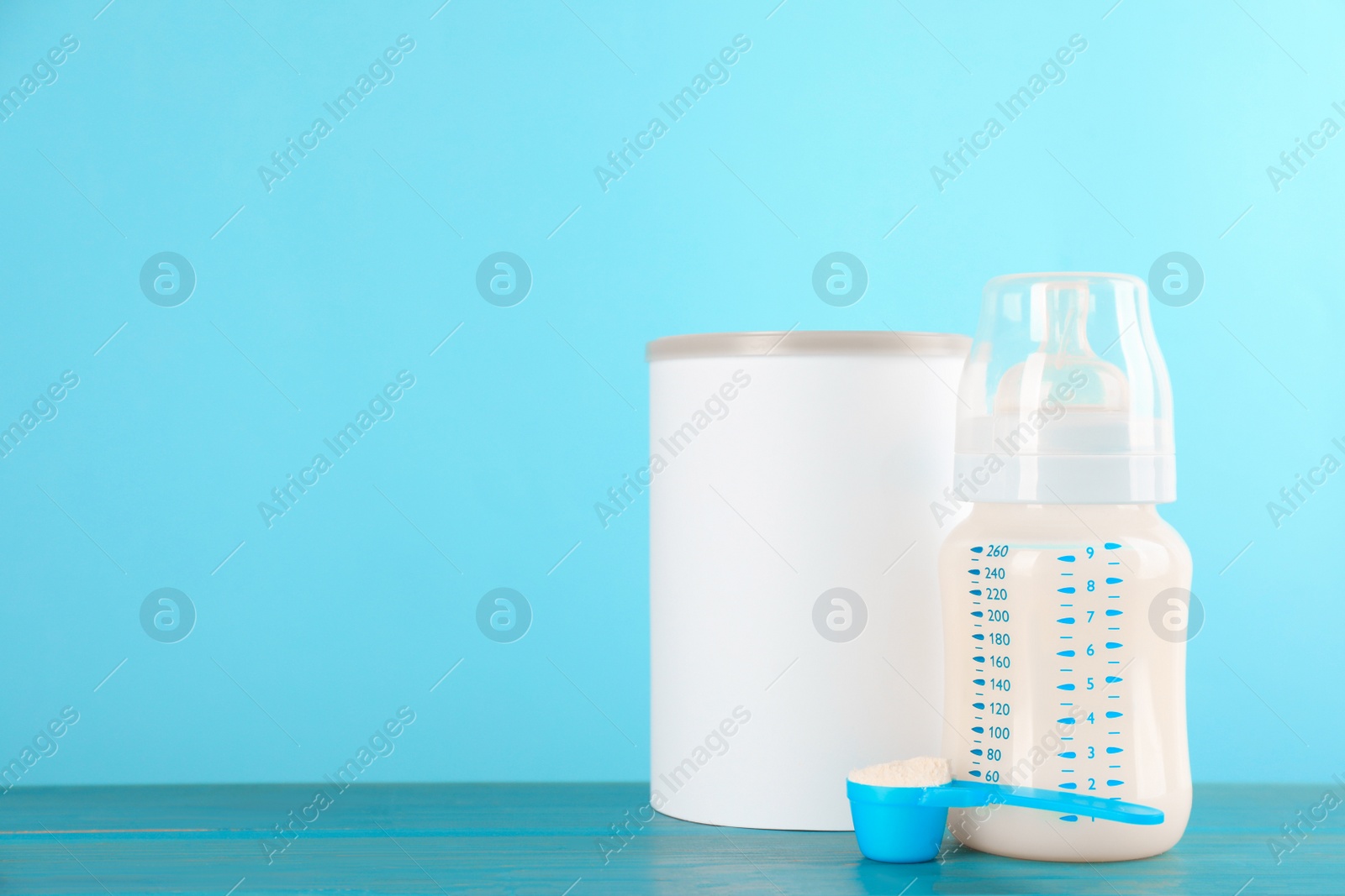 Photo of Blank can of powdered infant formula, feeding bottle and scoop on turquoise wooden table, space for text