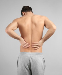 Young man suffering from back pain on grey background