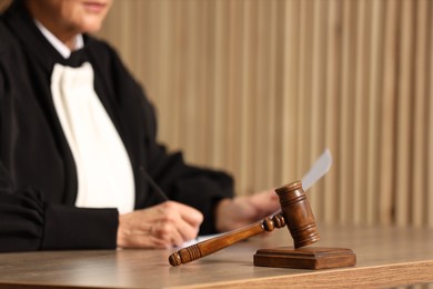 Photo of Judge working with document indoors, selective focus. Mallet on wooden table, closeup