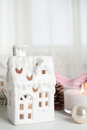 Composition with candle in house shaped holder on white wooden table. Christmas decoration