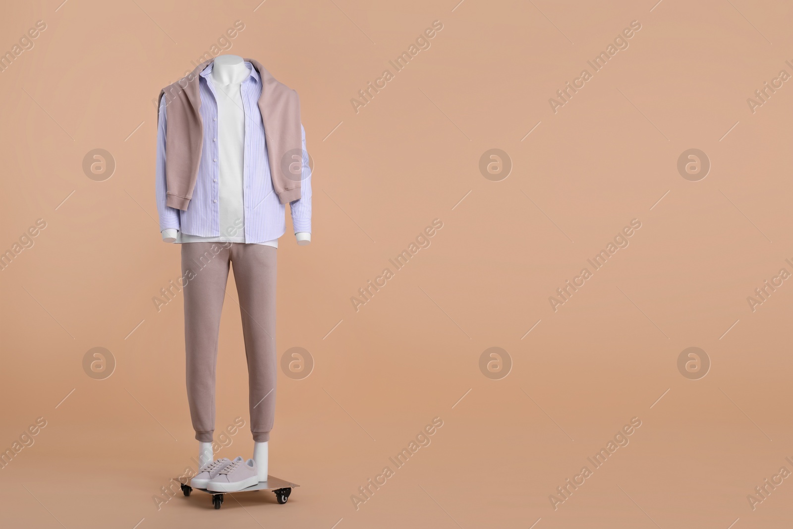 Photo of Male mannequin with sneakers dressed in white t-shirt, sweater, striped shirt and pants on beige background, space for text