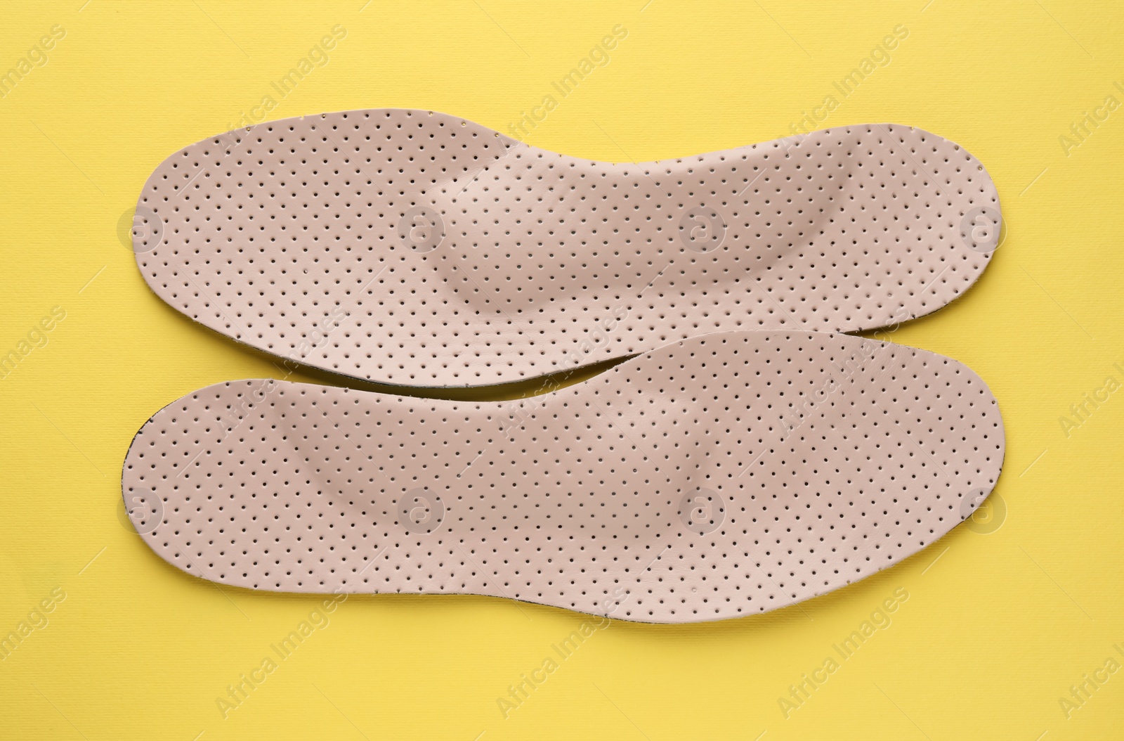 Photo of Beige orthopedic insoles on yellow background, flat lay