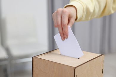 Photo of Woman putting her vote into ballot box on blurred background, closeup