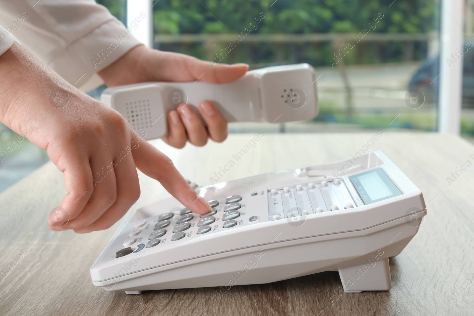 Photo of Woman dialing number on telephone at table indoors, closeup