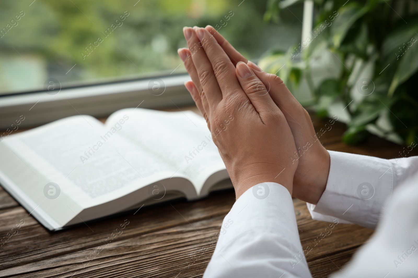 Photo of Woman holding hands clasped while praying at wooden table with Bible, closeup. Space for text