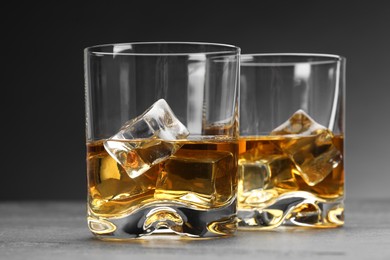 Photo of Whiskey and ice cubes in glasses on grey table, closeup