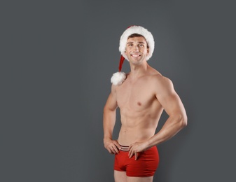 Photo of Young muscular man in Santa hat on gray background