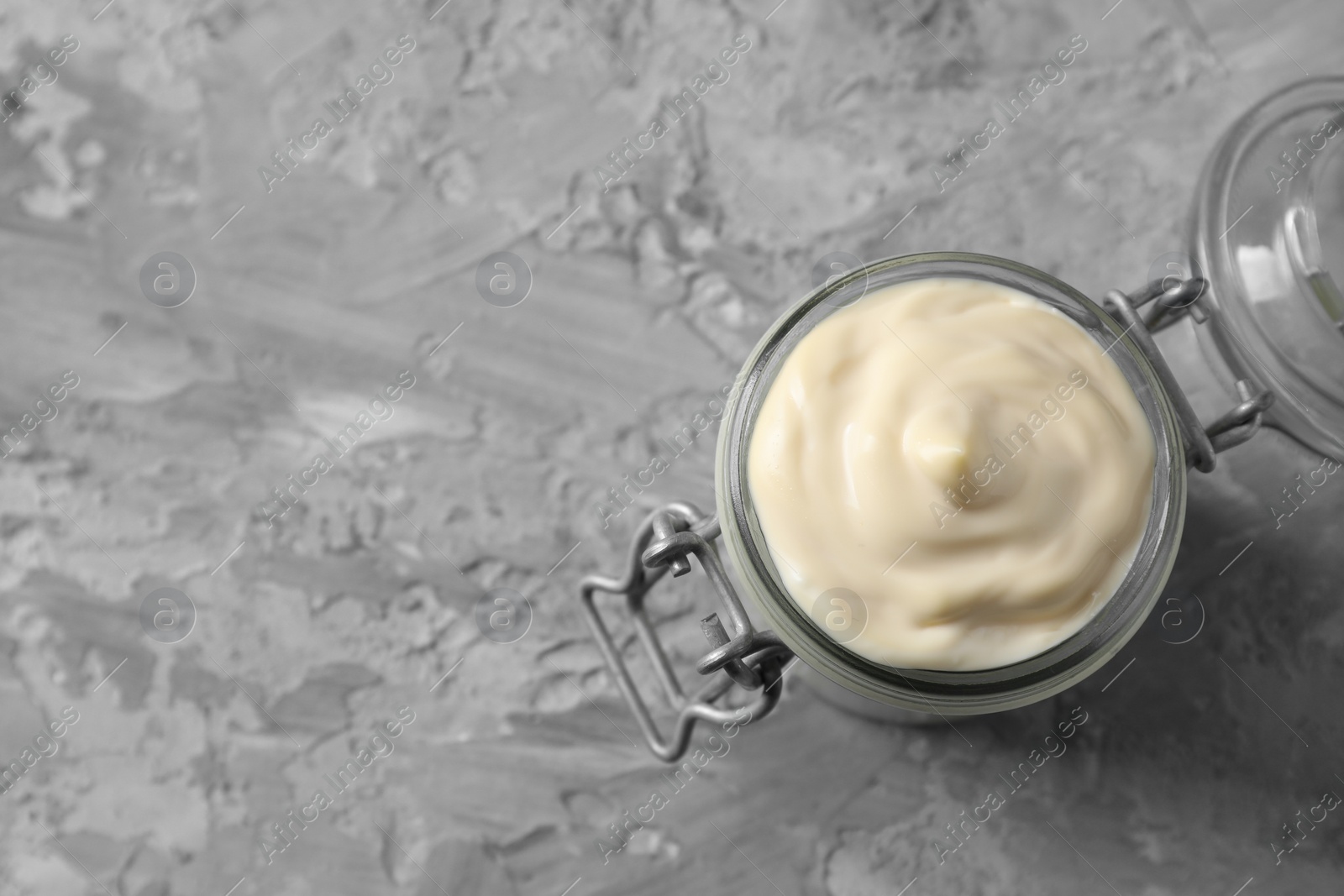 Photo of Tasty mayonnaise in jar on gray textured table, top view. Space for text