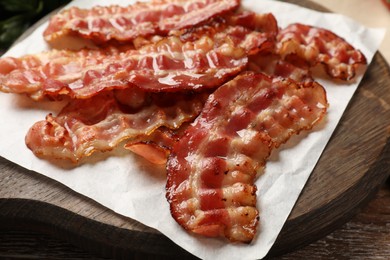 Photo of Board with fried bacon slices on wooden table, closeup