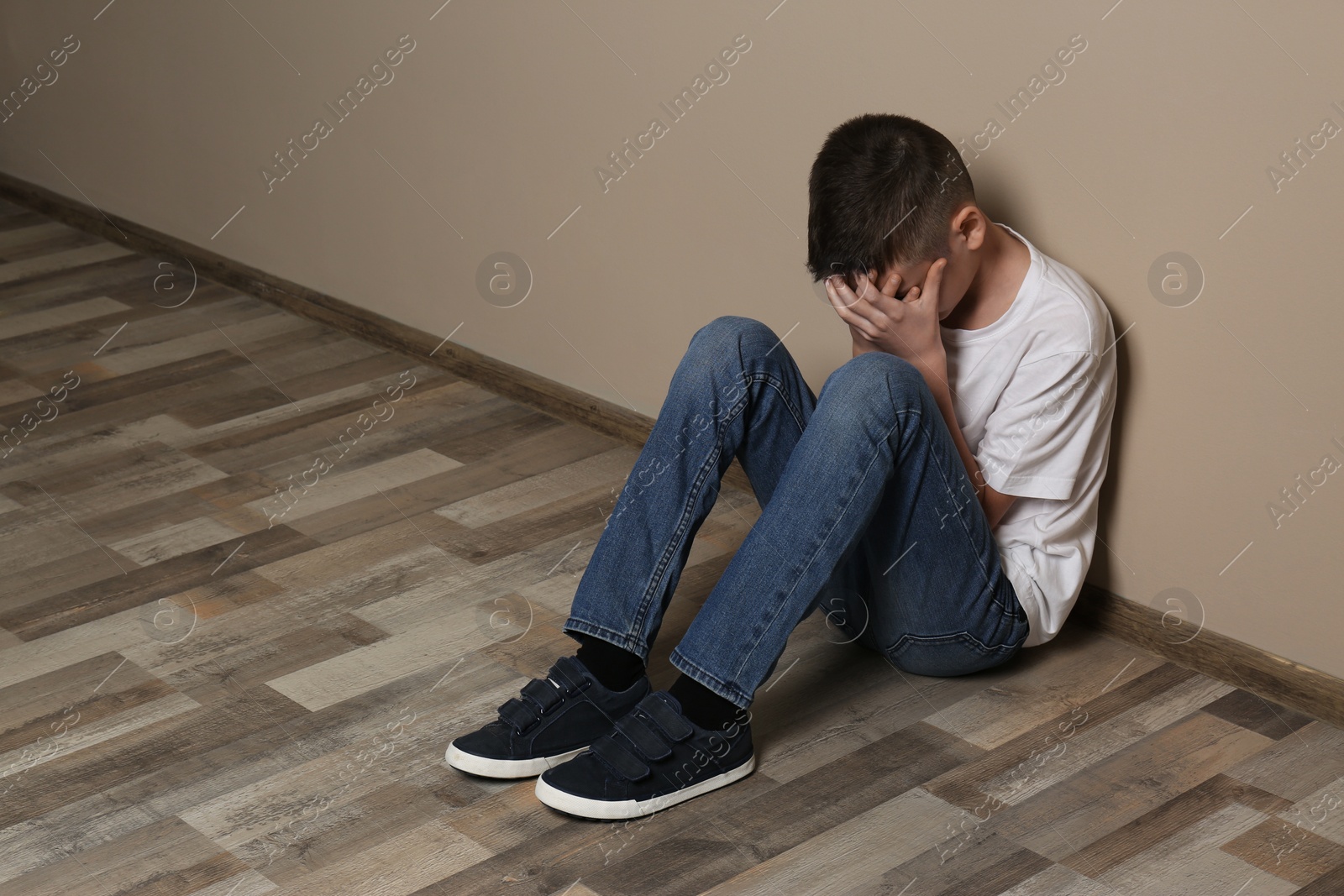 Photo of Upset boy sitting on floor at color wall. Space for text