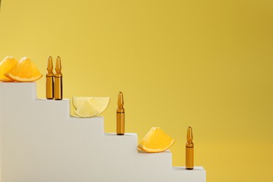 Photo of Stylish presentation of skincare ampoules with vitamin C and citrus slices on decorative stairs against yellow background, closeup. Space for text
