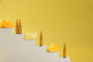 Stylish presentation of skincare ampoules with vitamin C and citrus slices on decorative stairs against yellow background, closeup. Space for text