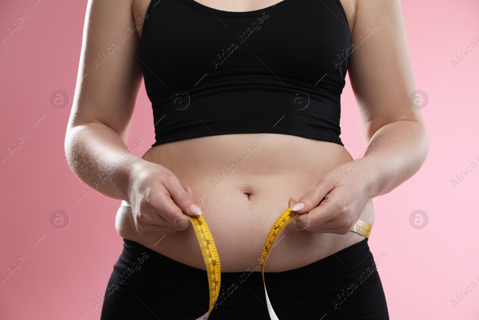 Photo of Woman measuring belly with tape on pink background, closeup. Overweight problem