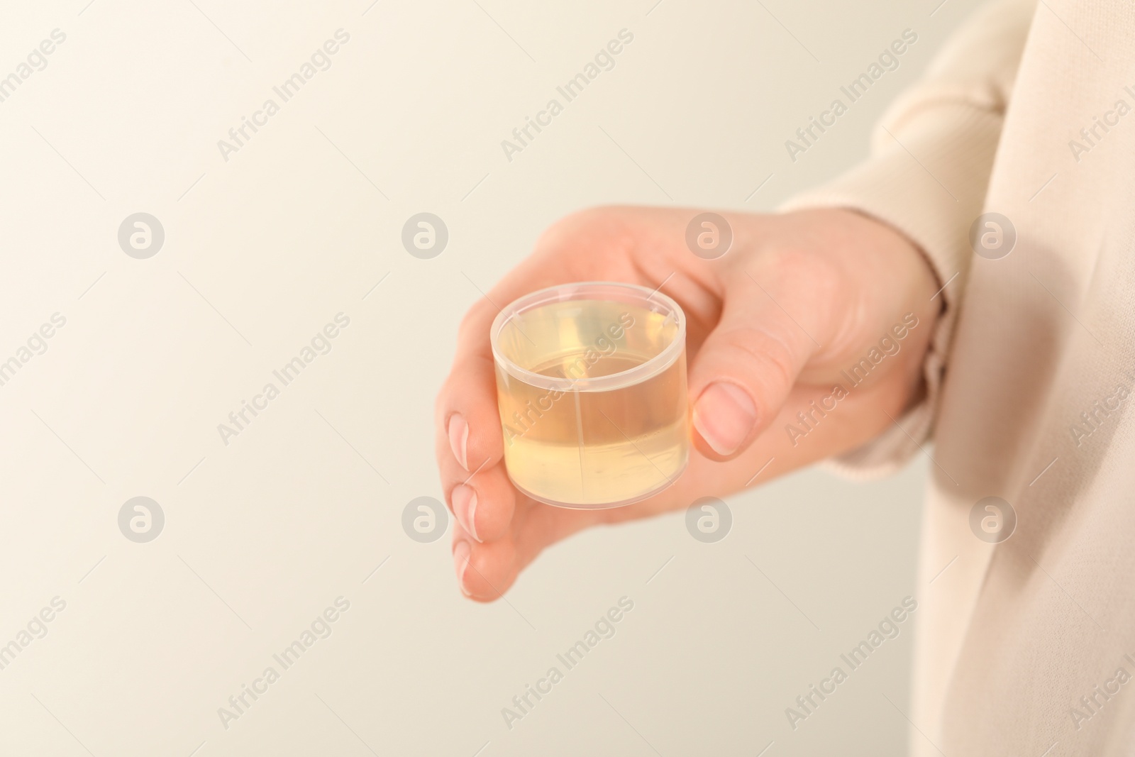 Photo of Woman holding measuring cup with syrup on light background, closeup. Cold medicine