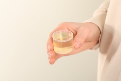 Woman holding measuring cup with syrup on light background, closeup. Cold medicine