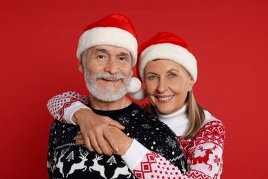 Photo of Senior couple in Christmas sweaters and Santa hats on red background