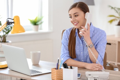 Photo of Young woman talking on phone at workplace