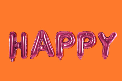 Word HAPPY made of pink foil balloons letters on orange background