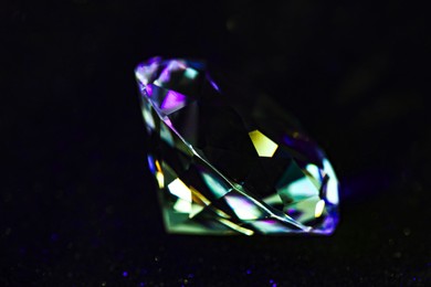 Photo of Beautiful dazzling diamond on black glitter surface, closeup