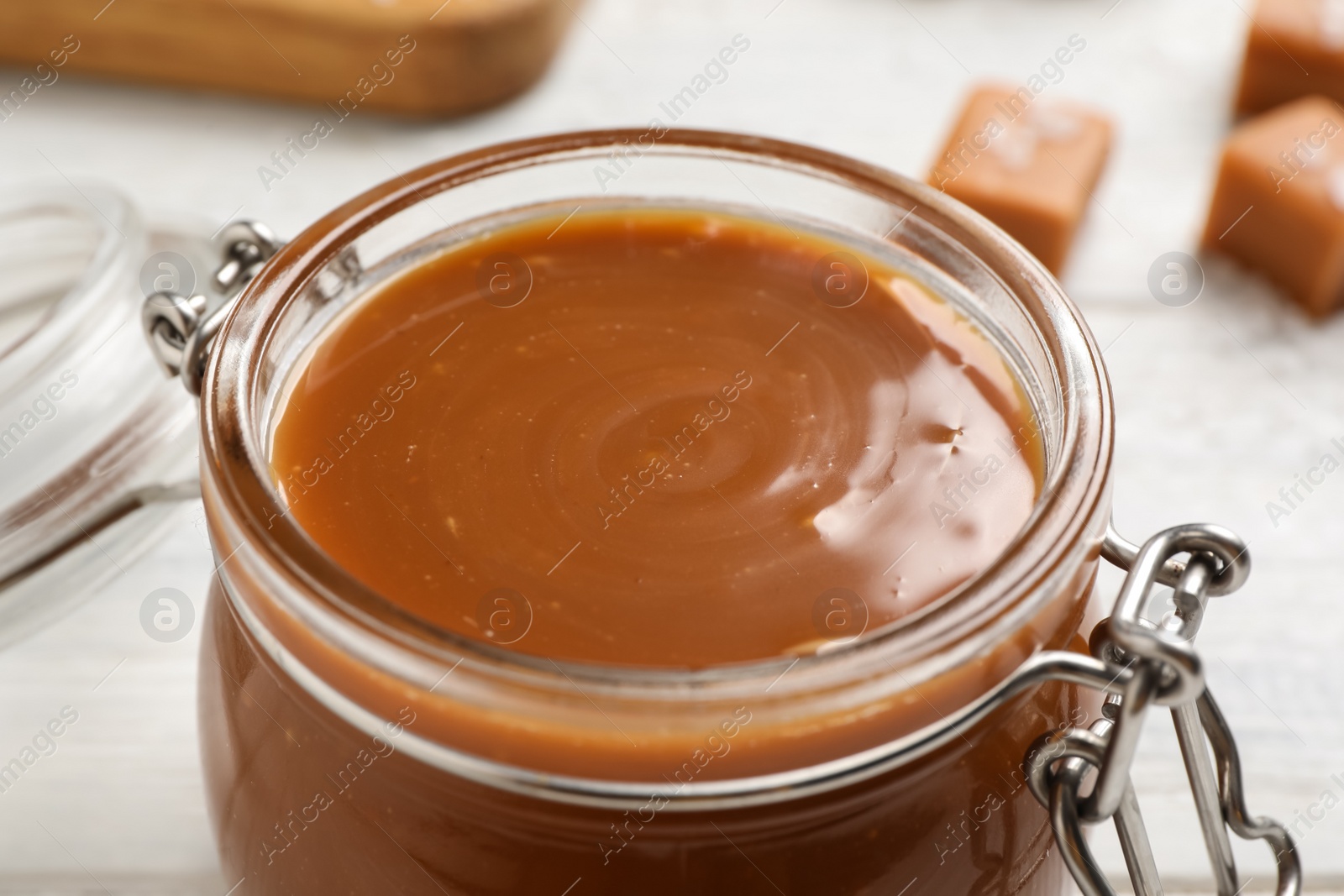 Photo of Yummy salted caramel in glass jar on white table, closeup