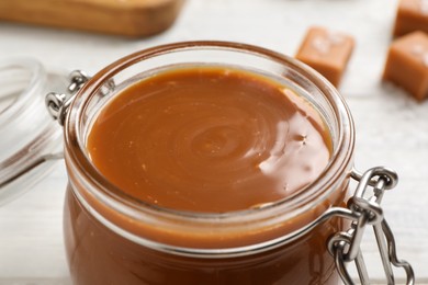 Yummy salted caramel in glass jar on white table, closeup