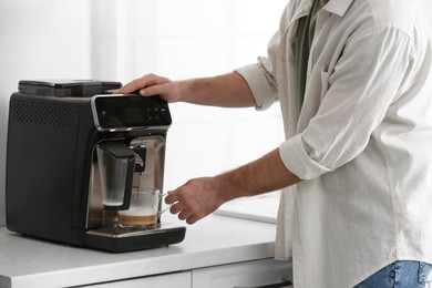 Young man preparing fresh aromatic coffee with modern machine in kitchen, closeup