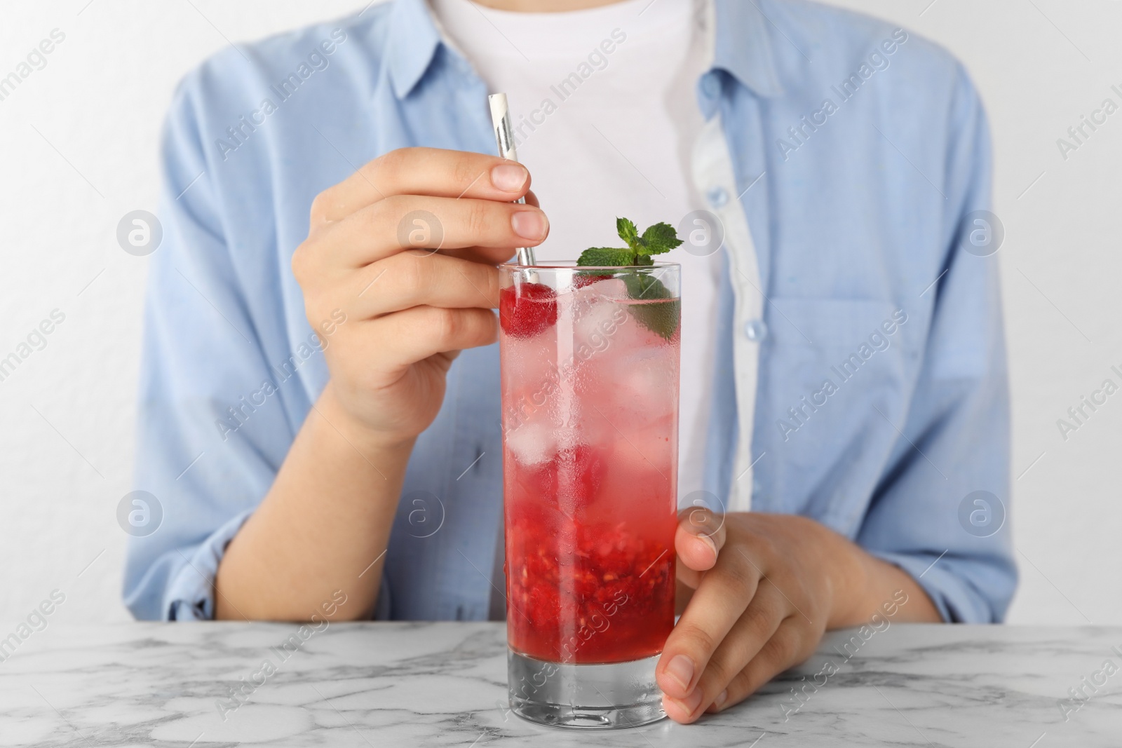 Photo of Woman with glass of raspberry refreshing drink at marble table, closeup