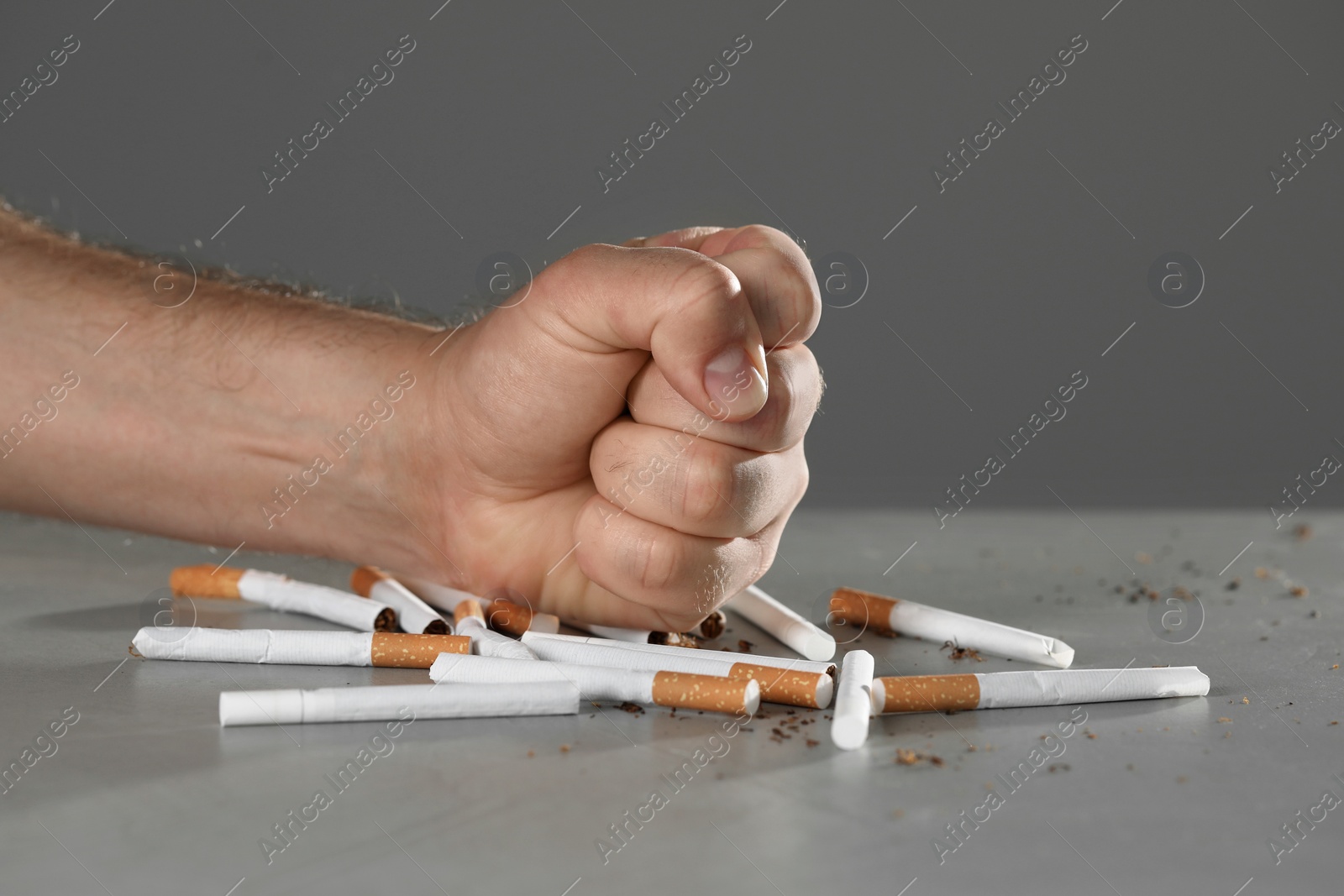 Photo of Stop smoking concept. Man crushing cigarettes at gray table, closeup