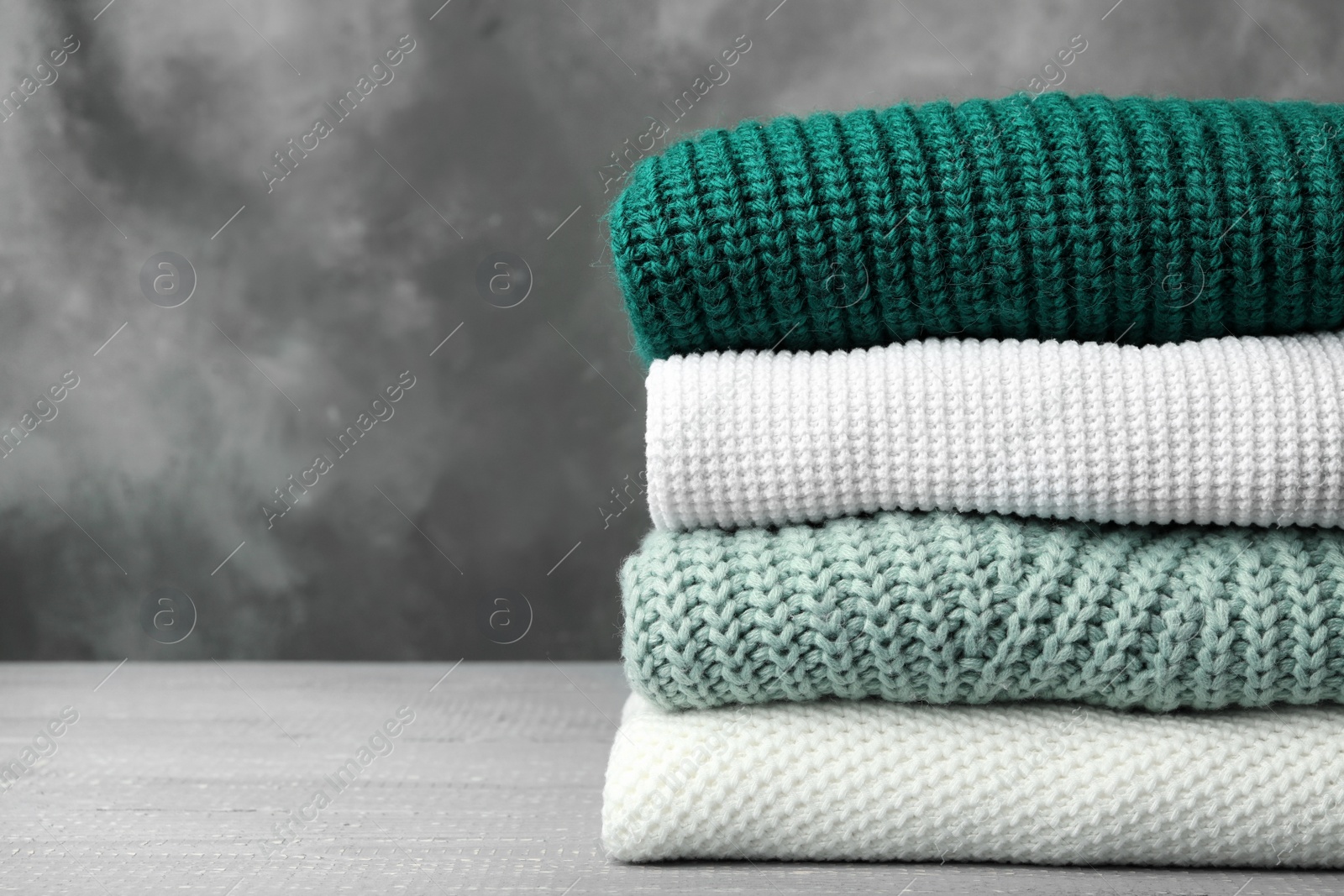 Photo of Stack of warm clothes on wooden table against grey background, space for text. Autumn season