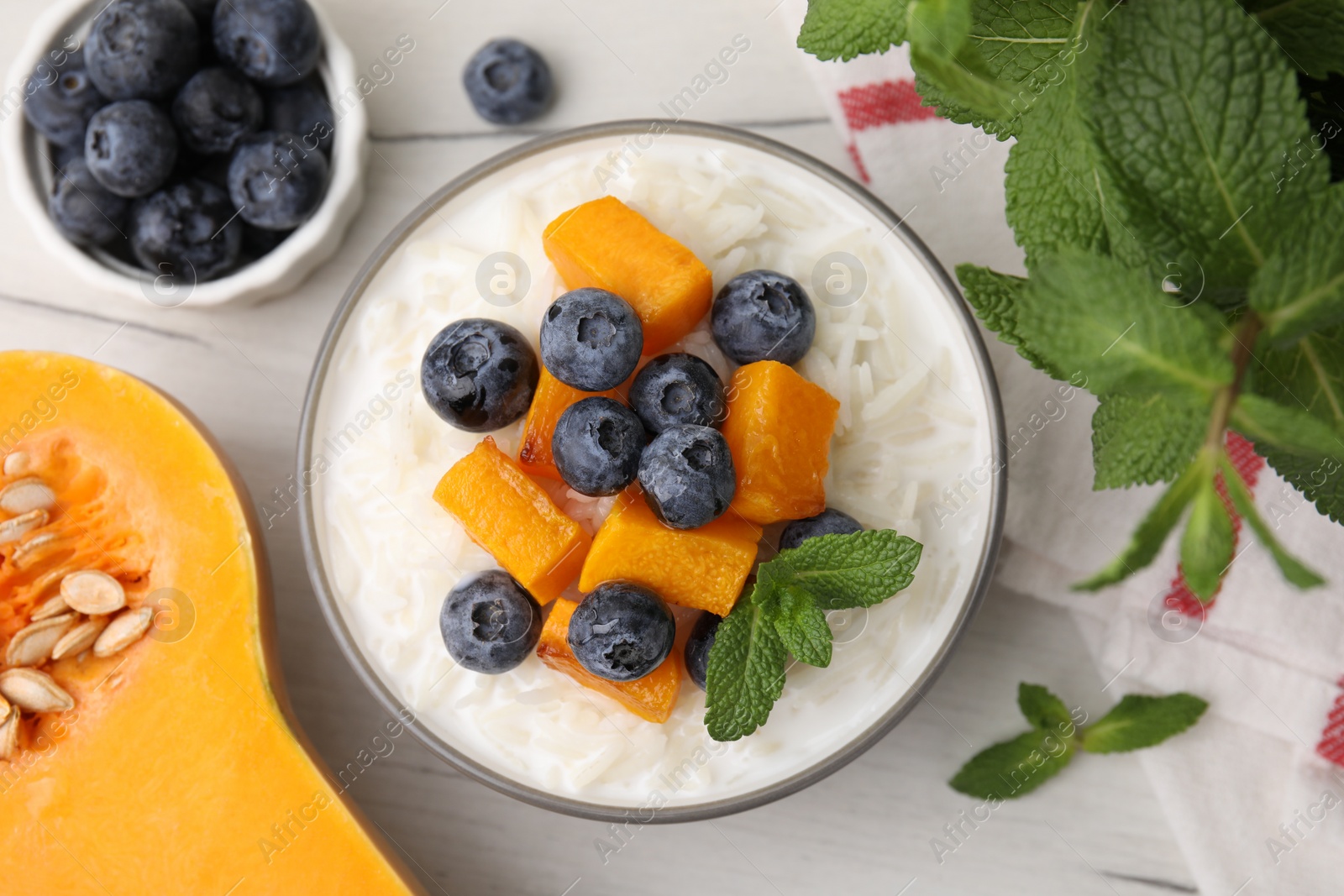 Photo of Bowl of delicious rice porridge with blueberries, pumpkin and mint on table, flat lay