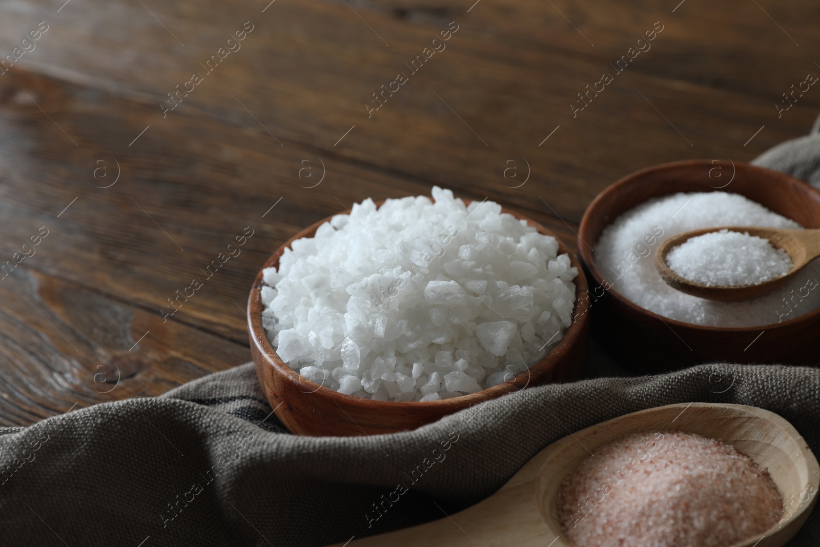 Photo of Different types of organic salt on wooden table, closeup