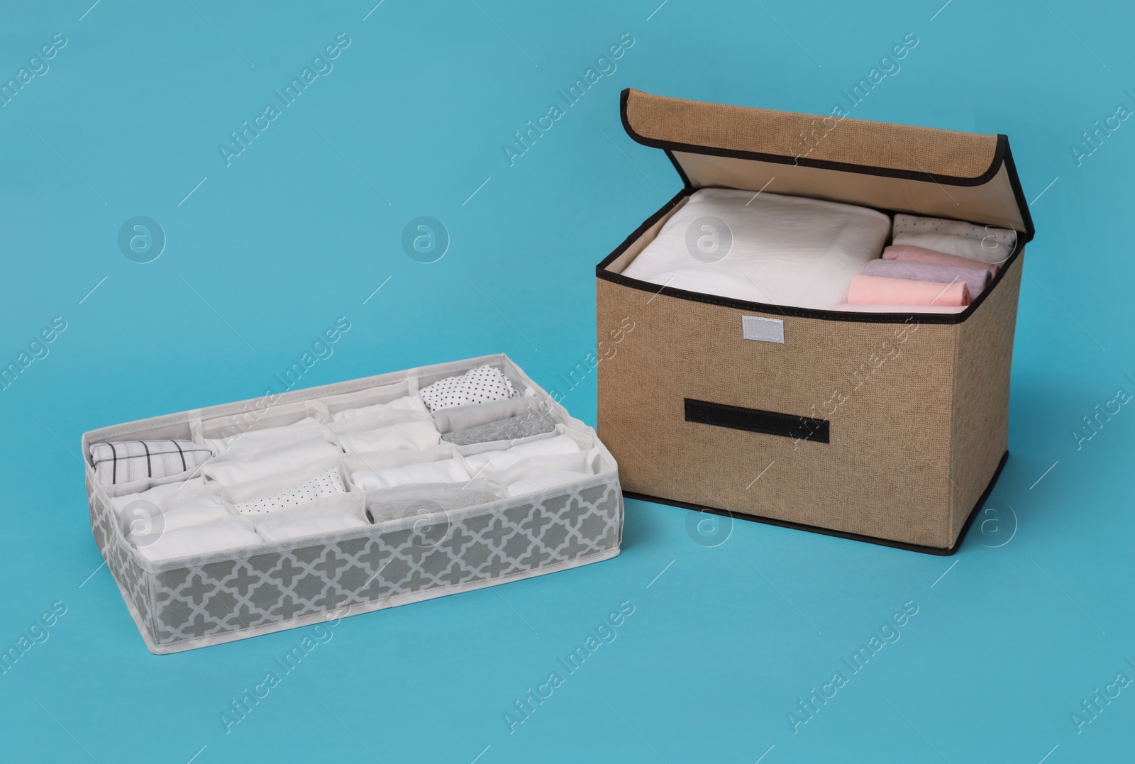 Photo of Textile storage case and organizer with folded clothes on light blue background