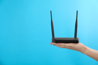 Photo of Woman holding modern Wi-Fi router on light blue background, closeup. Space for text