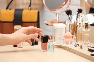 Photo of Woman reaching for cosmetic products on dressing table, closeup. Professional makeup