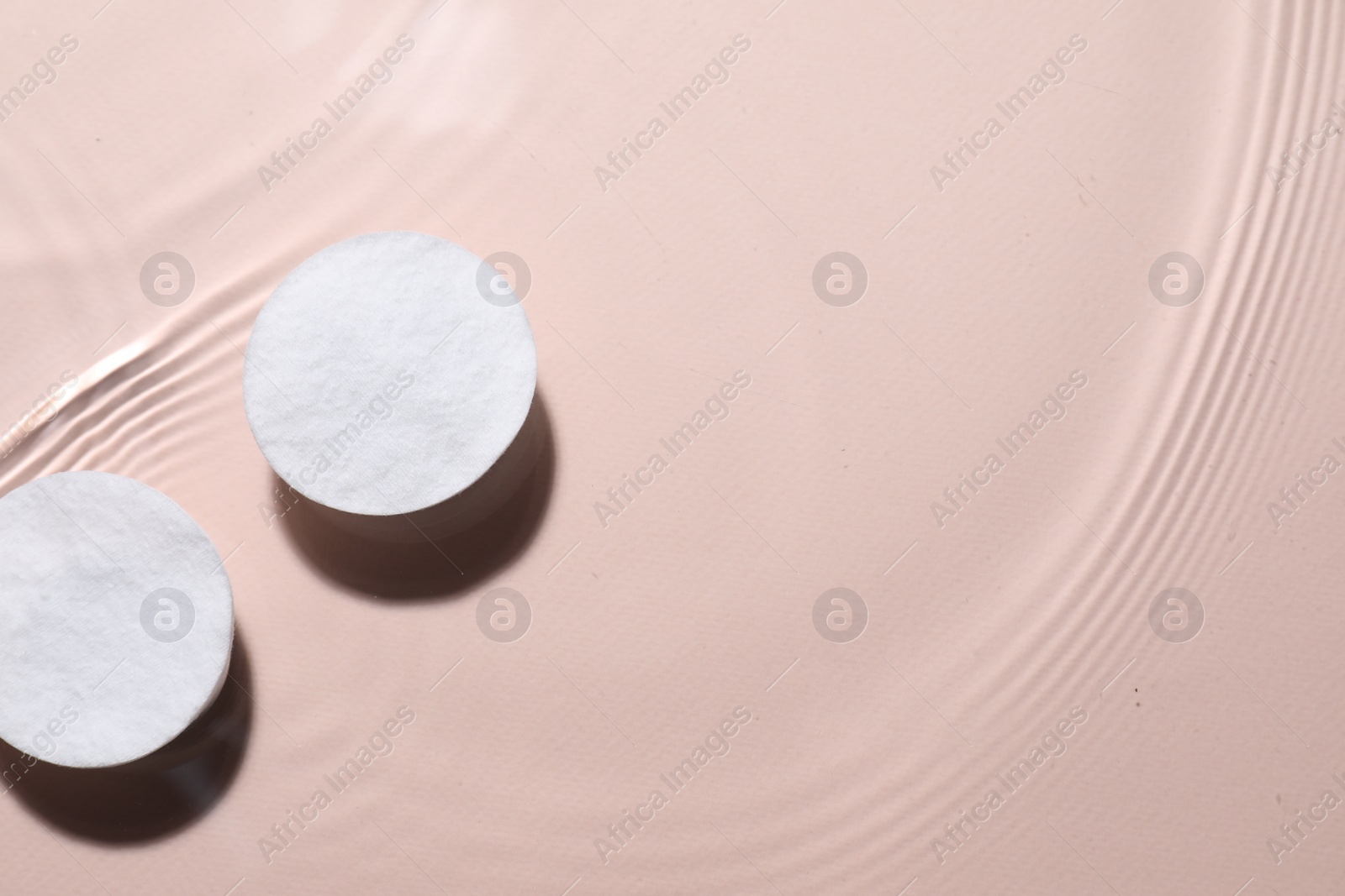 Photo of Cotton pads in micellar water on beige background, top view. Space for text