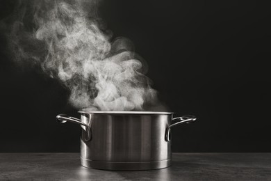 Photo of Steaming saucepot on grey table against dark background
