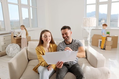 Photo of Family settling into home. Happy wife with husband choosing interior details while daughter and son unpacking boxes in new apartment. Moving day