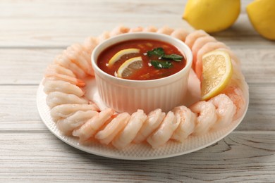 Photo of Tasty boiled shrimps with cocktail sauce and lemon on white wooden table