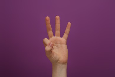 Photo of Woman showing three fingers on purple background, closeup