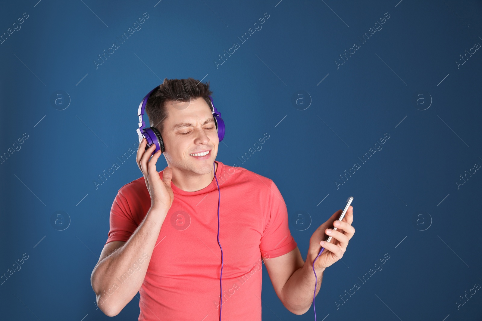 Photo of Man in headphones with mobile device on color background. Space for text