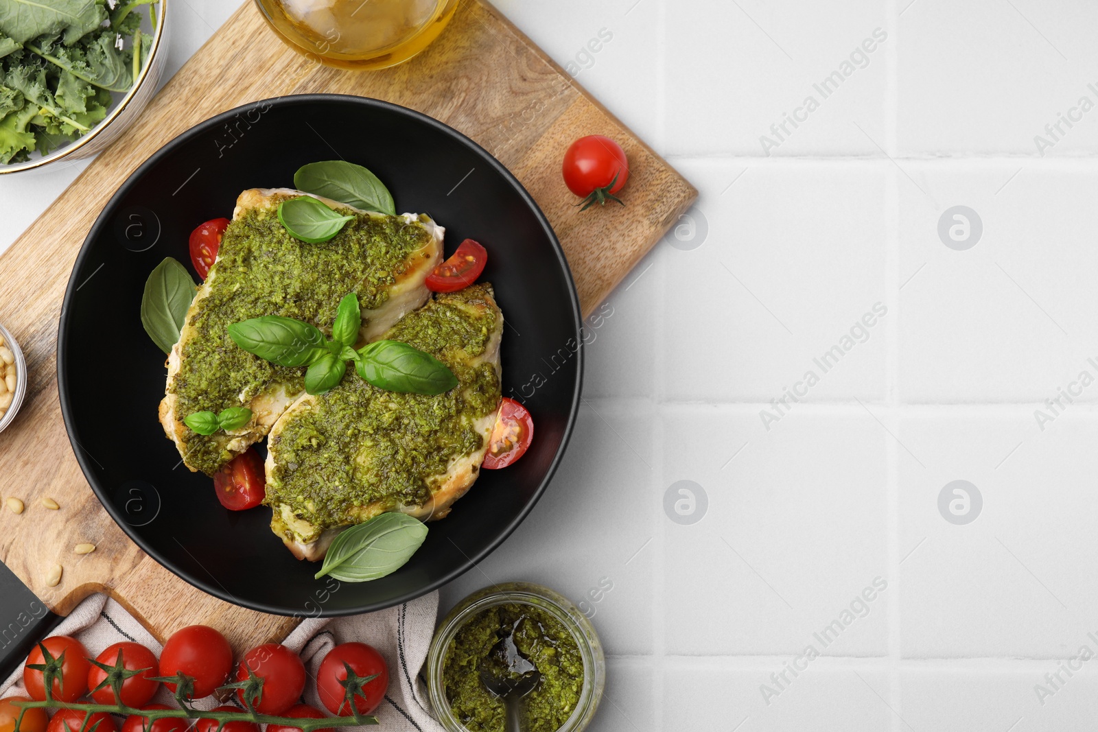 Photo of Delicious chicken breasts with pesto sauce and ingredients on white tiled table, flat lay. Space for text