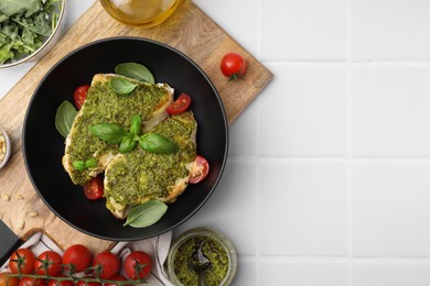 Delicious chicken breasts with pesto sauce and ingredients on white tiled table, flat lay. Space for text