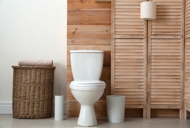 Photo of Toilet bowl near wooden wall in modern bathroom interior