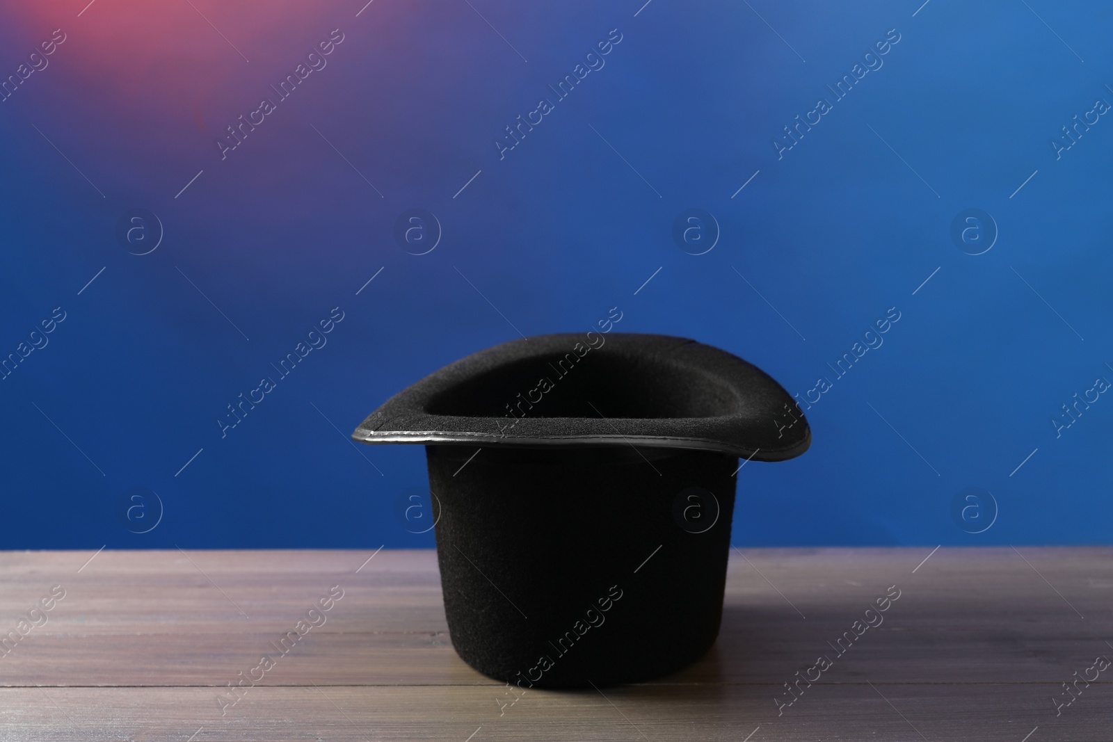 Photo of Magician's hat on wooden table against color background