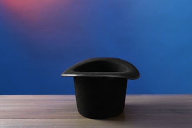 Photo of Magician's hat on wooden table against color background