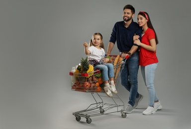 Photo of Happy family with shopping cart full of groceries on grey background