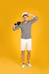 Photo of Serious sailor man with binoculars on yellow background