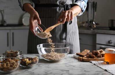 Photo of Woman preparing healthy granola bar at white marble table in kitchen, closeup